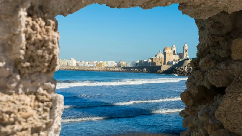 The cathedral and sea front of Cádiz seen through a rock arch, Spain