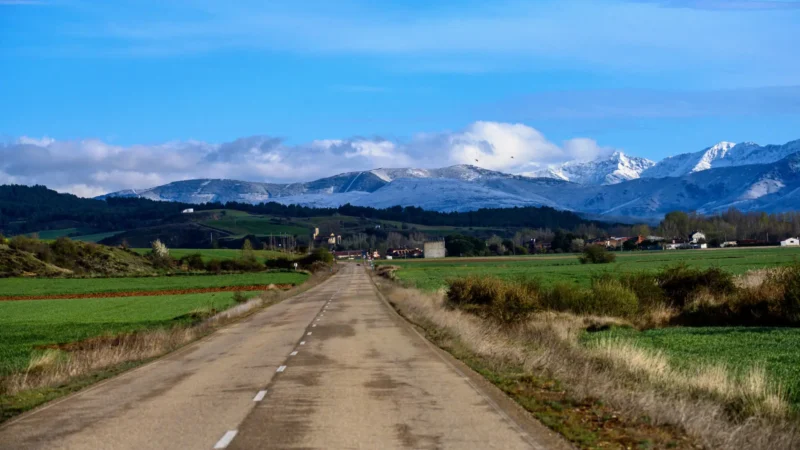 Empty road crossing the Castilian plains toward snow-capped mountains