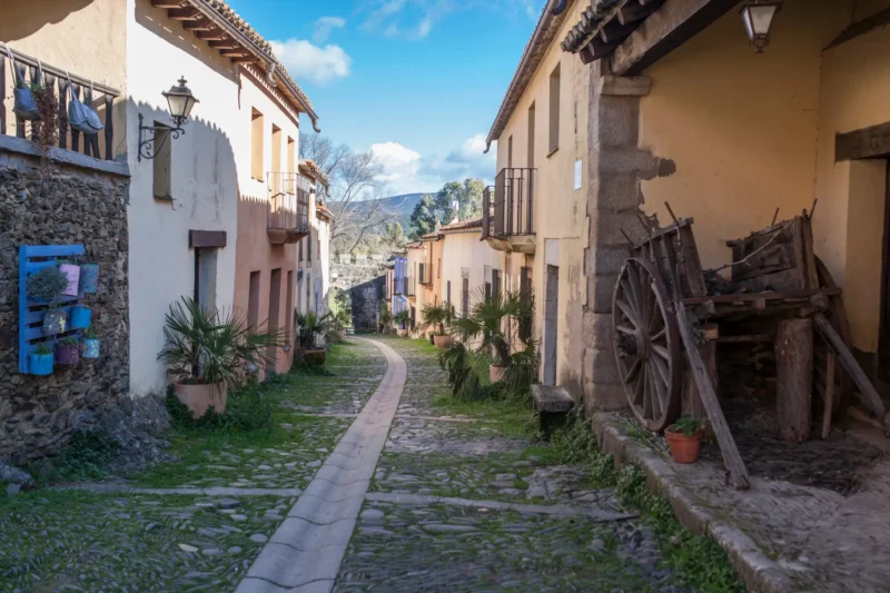 An empty cobbled street winding through the restored village of Granadilla in Extremadura, with an old wooden cart against a stone house
