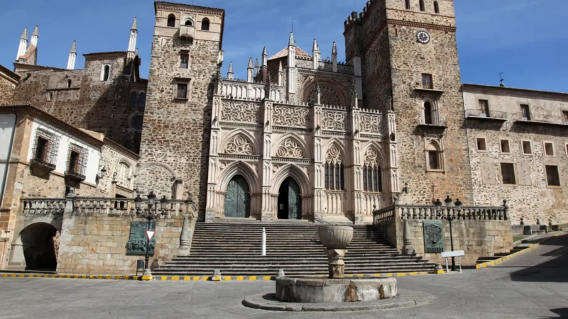 Gothic-Mudejar facade of the Royal Monastery of Guadalupe rising above the Plaza de Santa María, with the old stone fountain in the foreground, Extremadura, Spain