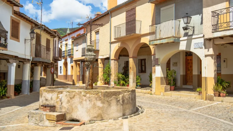 Fuente de los Tres Caños, a 15th-century stone fountain with a wrought-iron cross, in an arcaded square in the old Jewish quarter of Guadalupe, Extremadura, Spain