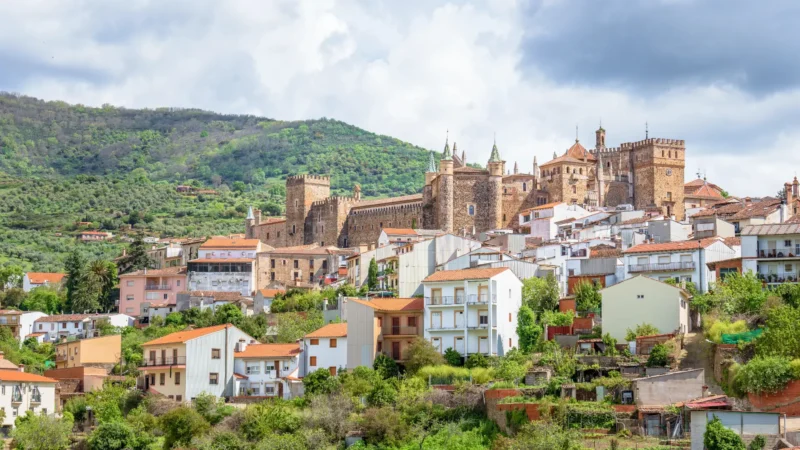 View of Guadalupe village with the towers of the Royal Monastery rising above the rooftops, set against the green Villuercas hills, Extremadura, Spain
