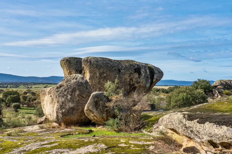 A large balancing granite boulder at Los Barruecos near Cáceres, with the open dehesa landscape behind