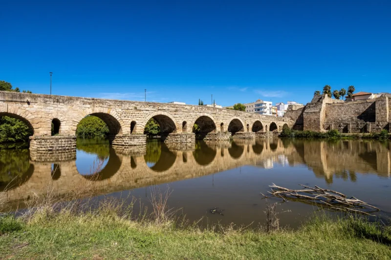 The full span of the Roman bridge at Mérida reflected in the Guadiana river, with the Alcazaba behind
