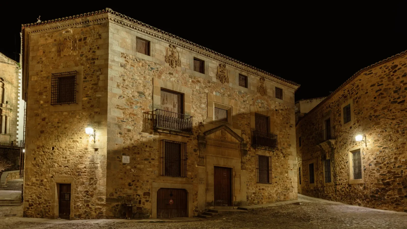 A floodlit stone palace on an empty street in the old town of Cáceres at night, Extremadura, Spain