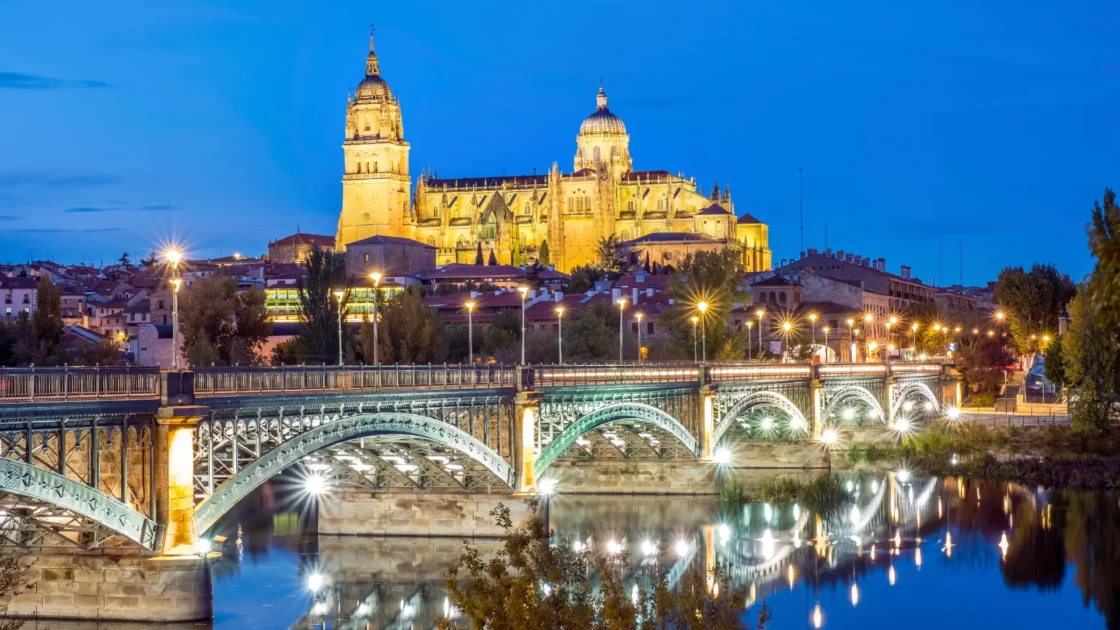 The floodlit cathedral and skyline of Salamanca above the Tormes river at dusk, Castilla y León, Spain