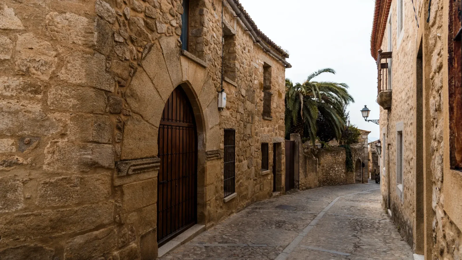 Quiet cobbled street with stone houses and an arched doorway in the old town of Trujillo