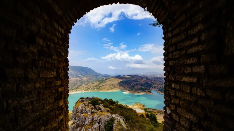 The turquoise reservoir seen through a stone window in the castle ruins, Zahara de la Sierra, Cádiz, Andalucía, Spain